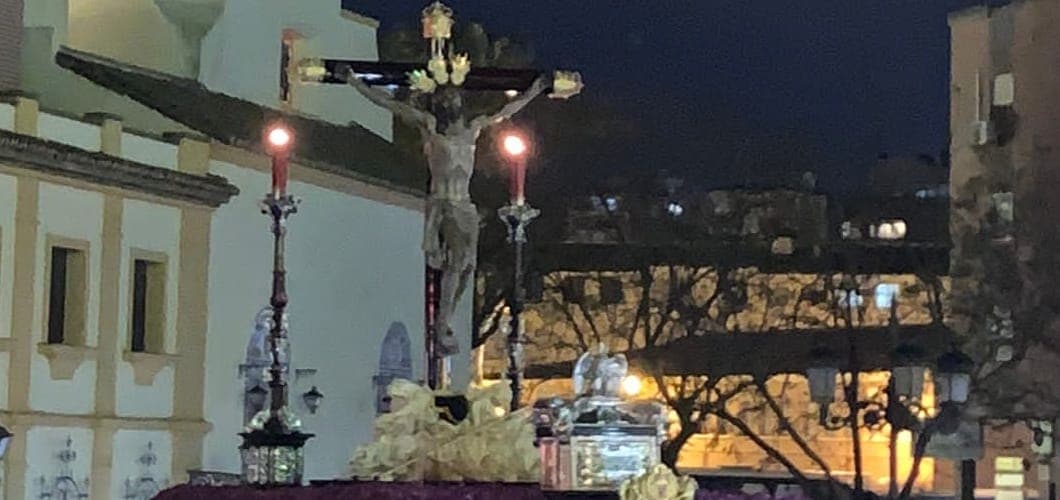 Procesión de Semana Santa por el centro histórico de Málaga, con nazarenos portando el trono bajo la luz de las velas