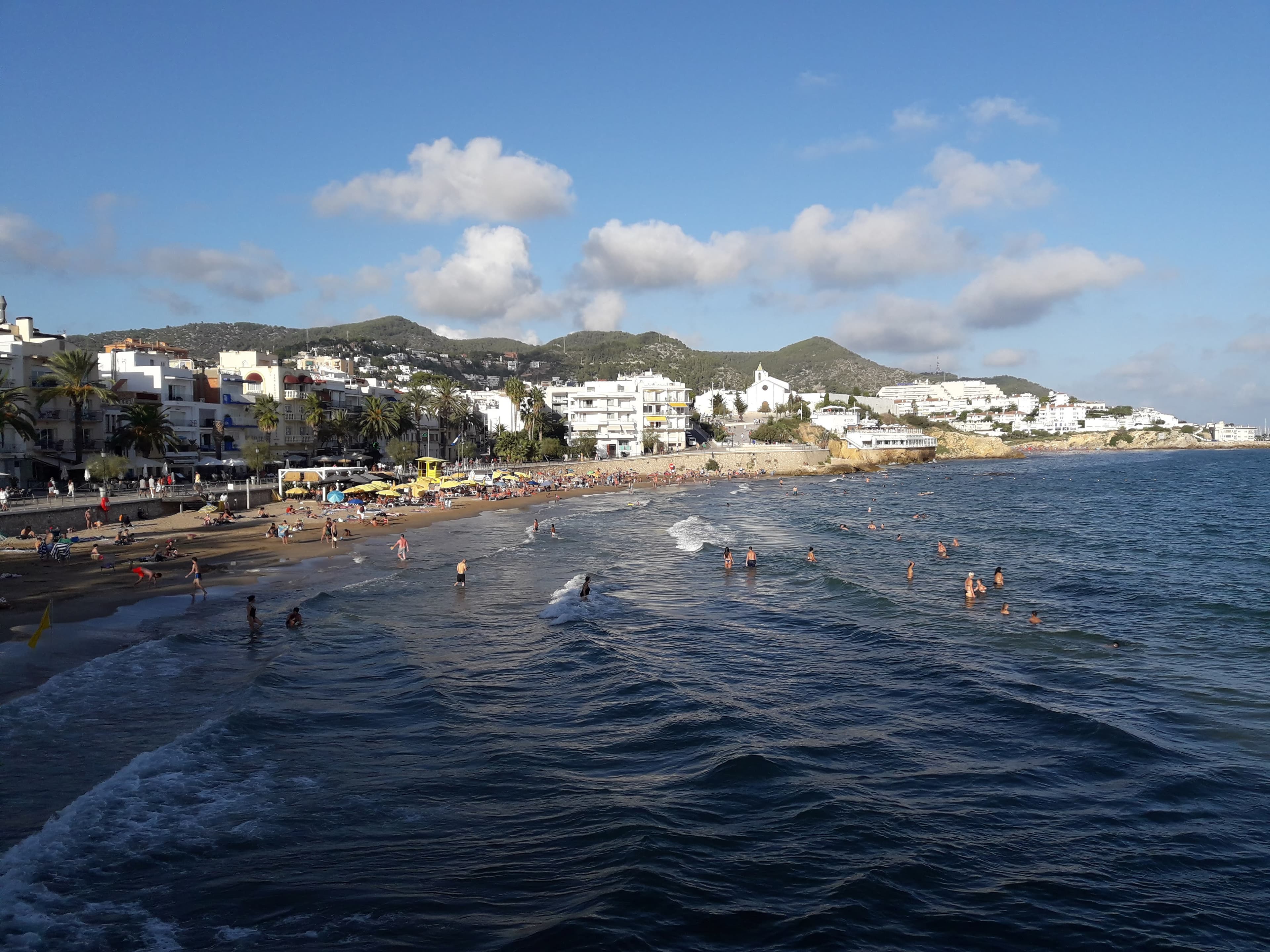 La tranquila Platja de Sant Sebastià de Sitges con barcas varadas y el campanario al fondo