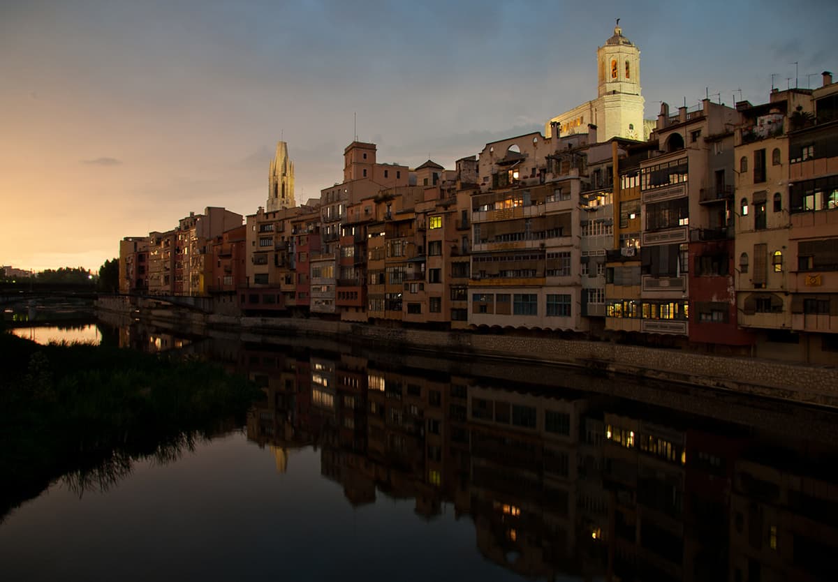 Casas de colores asomadas al río Onyar reflejándose en el agua al anochecer, en el casco antiguo de Girona
