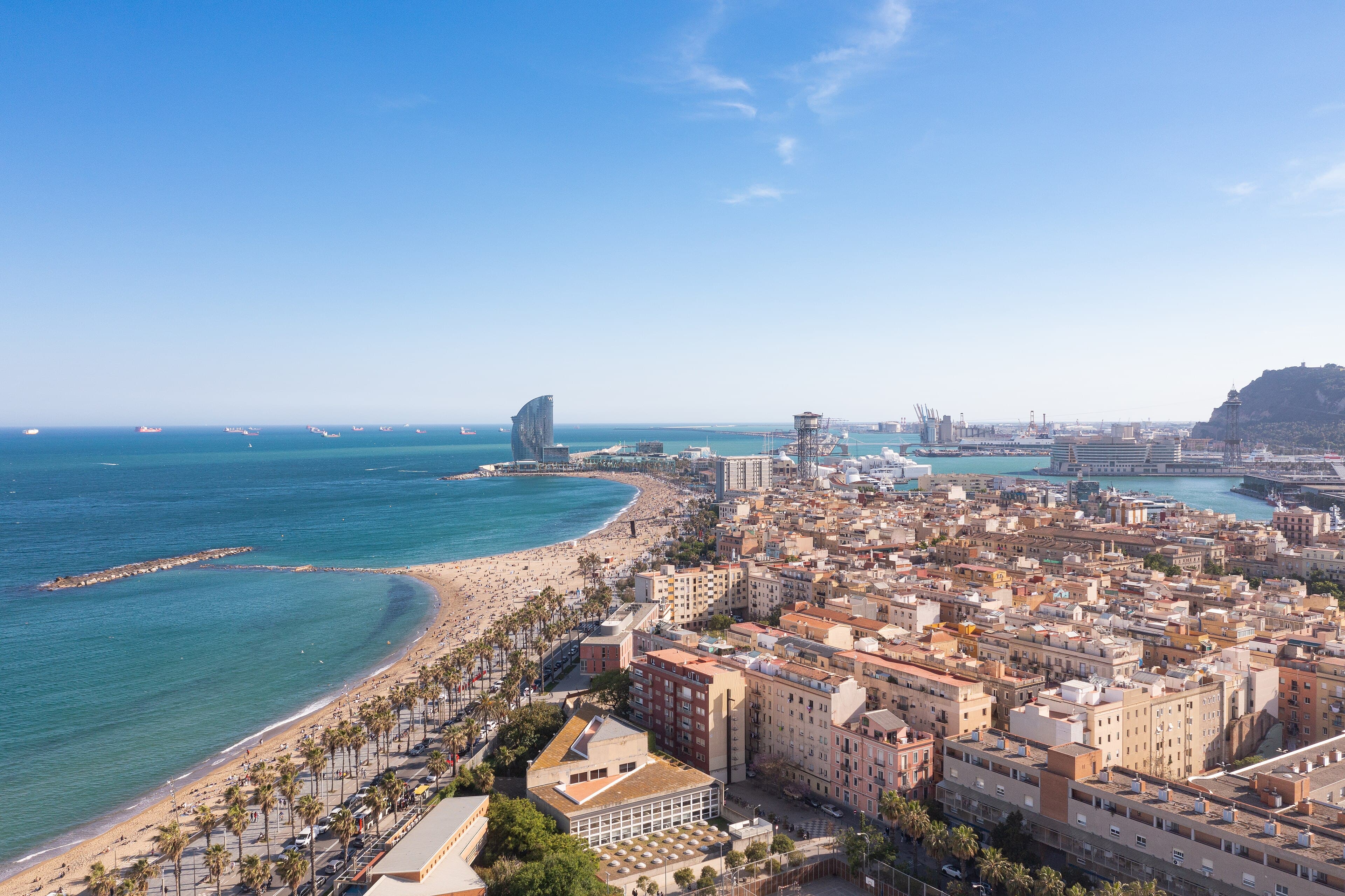 Vista aérea de la playa de la Barceloneta y el Port Vell, con la franja de arena, el paseo marítimo y el Mediterráneo junto al tejido urbano de Barcelona